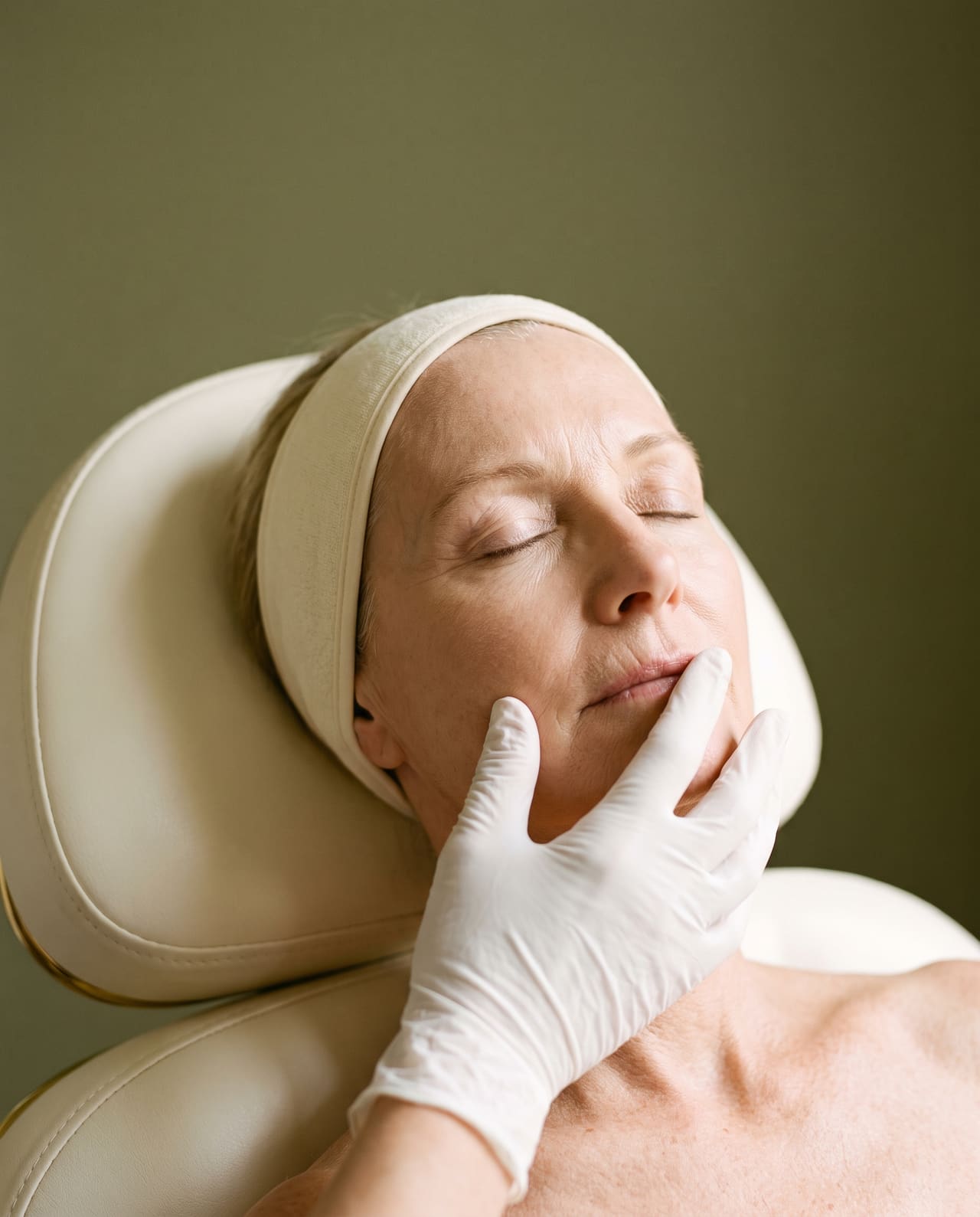 Gloved fingertips resting on the skin above the upper lip of a mature client with a cream headband.